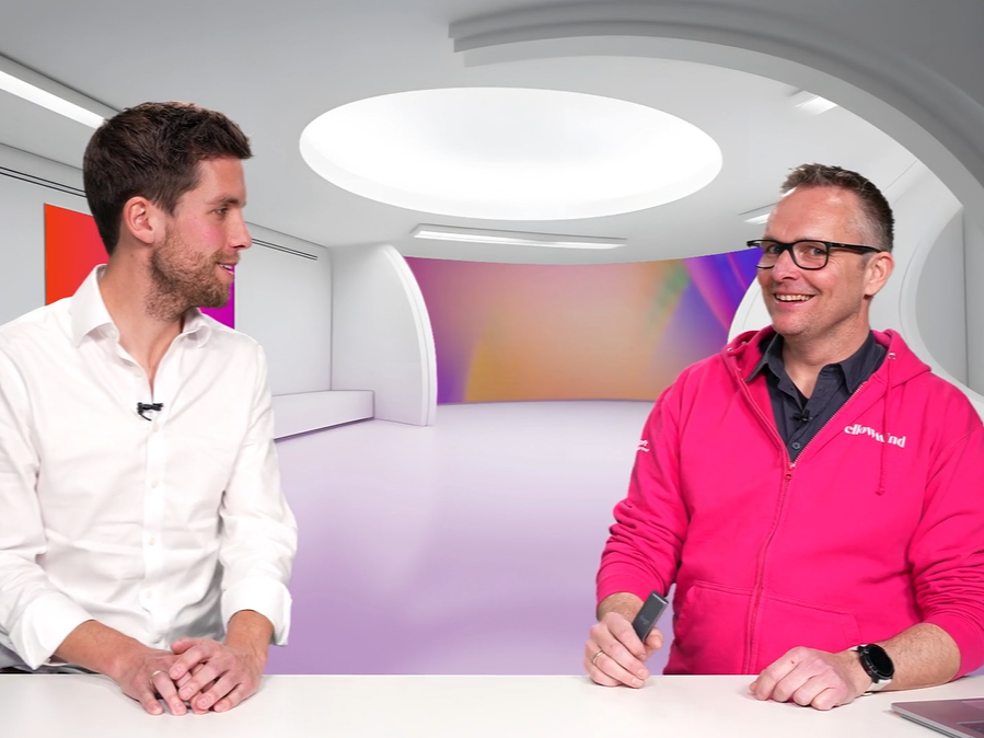 Twee mannen in een moderne studio aan een tafel, met een kleurrijke achtergrond en witte inrichting