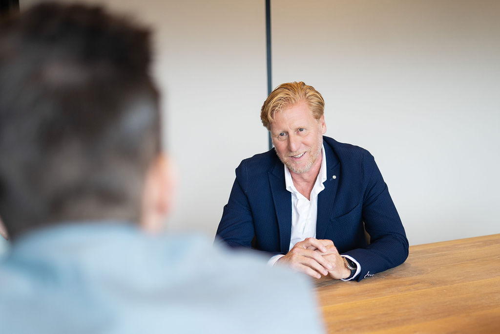 Twee mannen in nette zakelijke kleding staan buiten voor een modern glazen gebouw en praten met elkaar