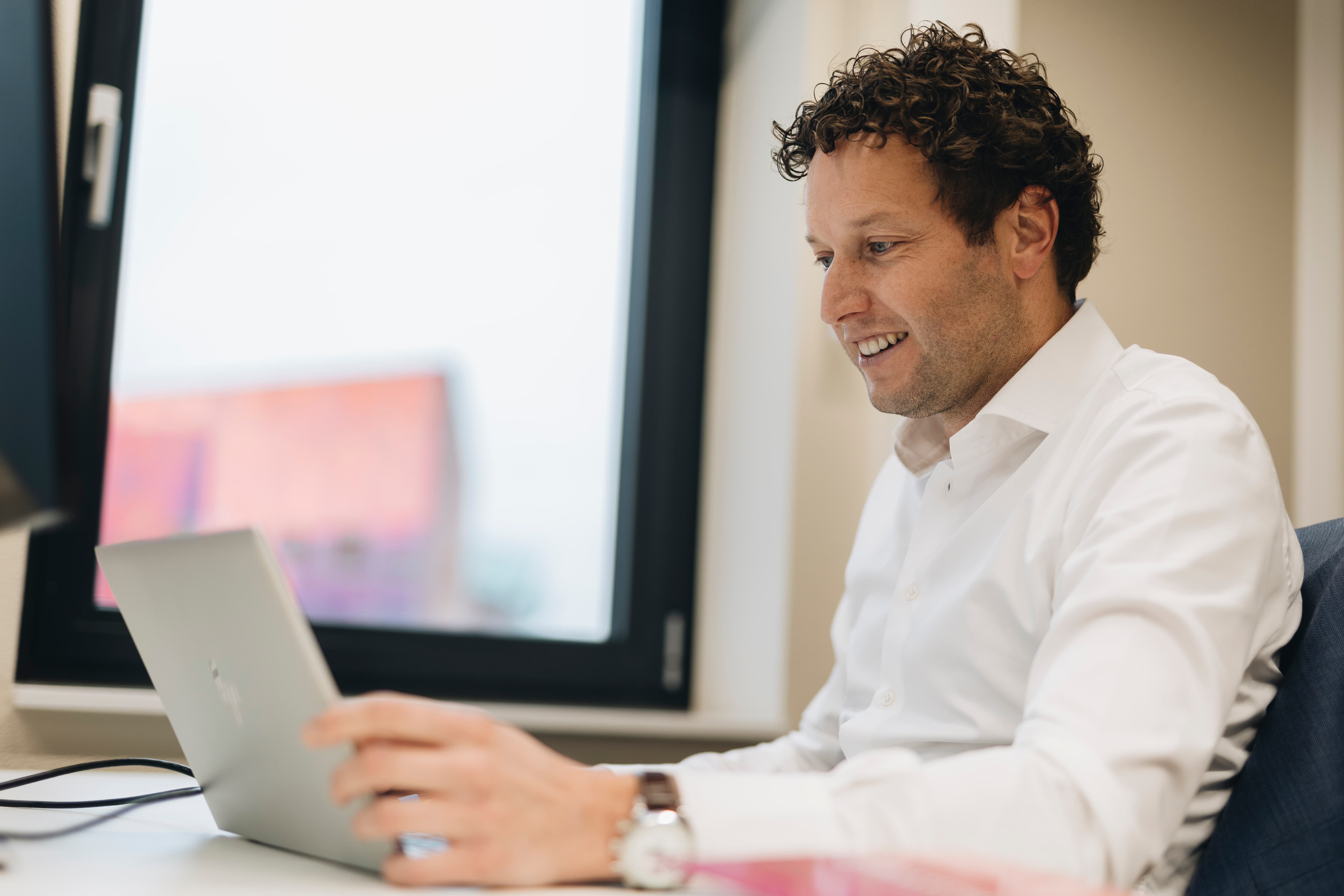 Man werkt op een laptop in een kantooromgeving, met wit overhemd en window light op de achtergrond