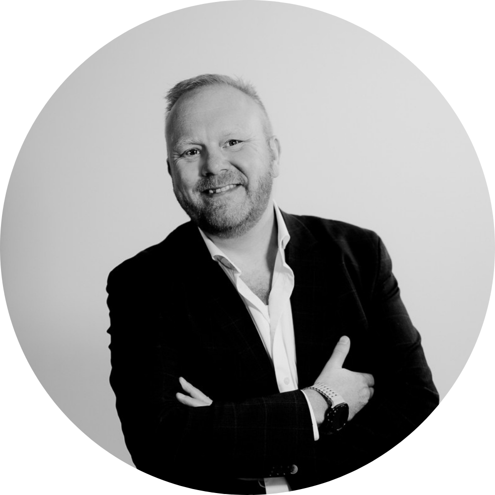 Sort-hvid portræt af Daniel Høgedahl i blazer og åben skjorte med armene krydset. Neutral businessprofil mod lys baggrund