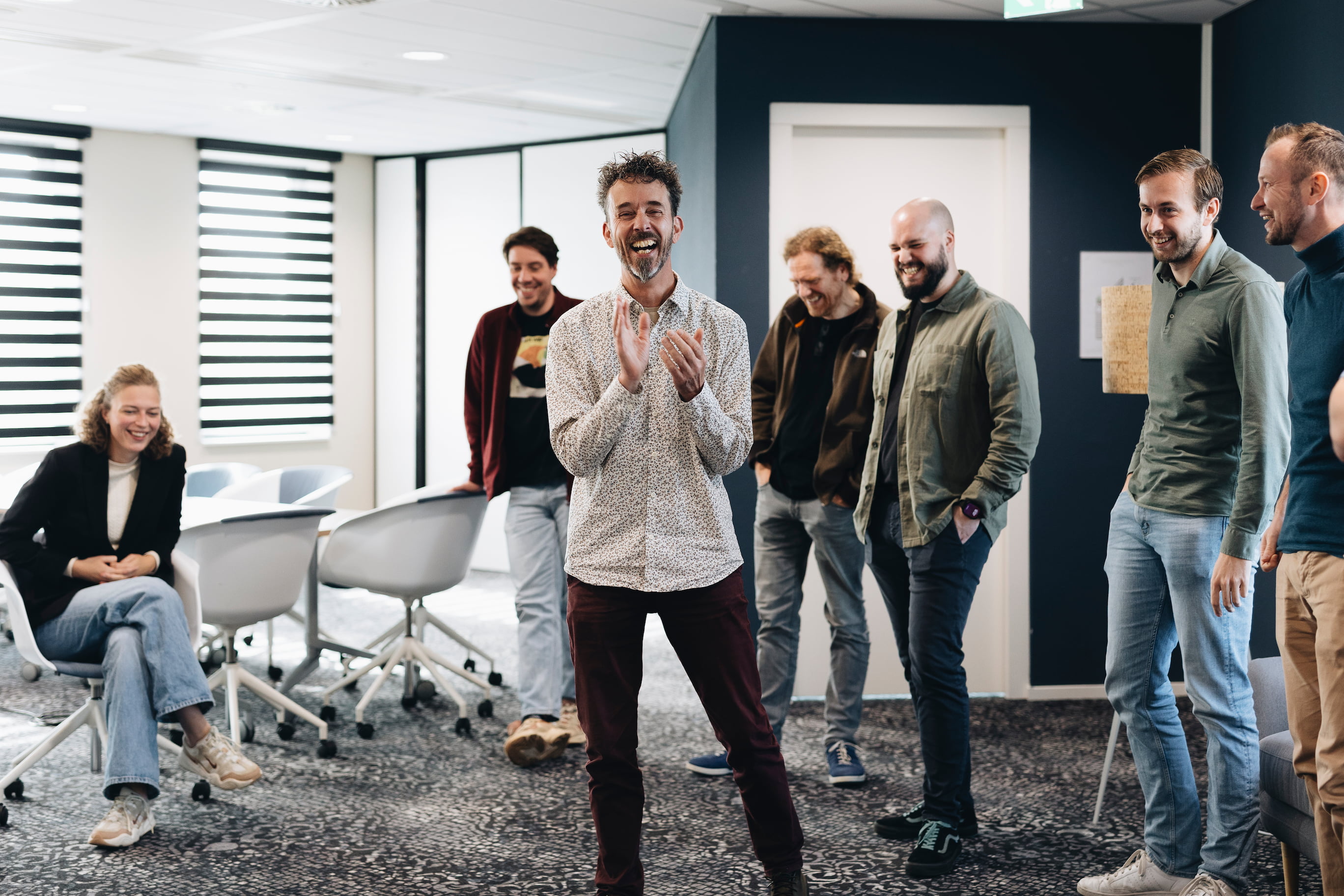 Groep collega's die in een kantoorvergadering staan en werk bespreken rond een bureau met computers en documenten