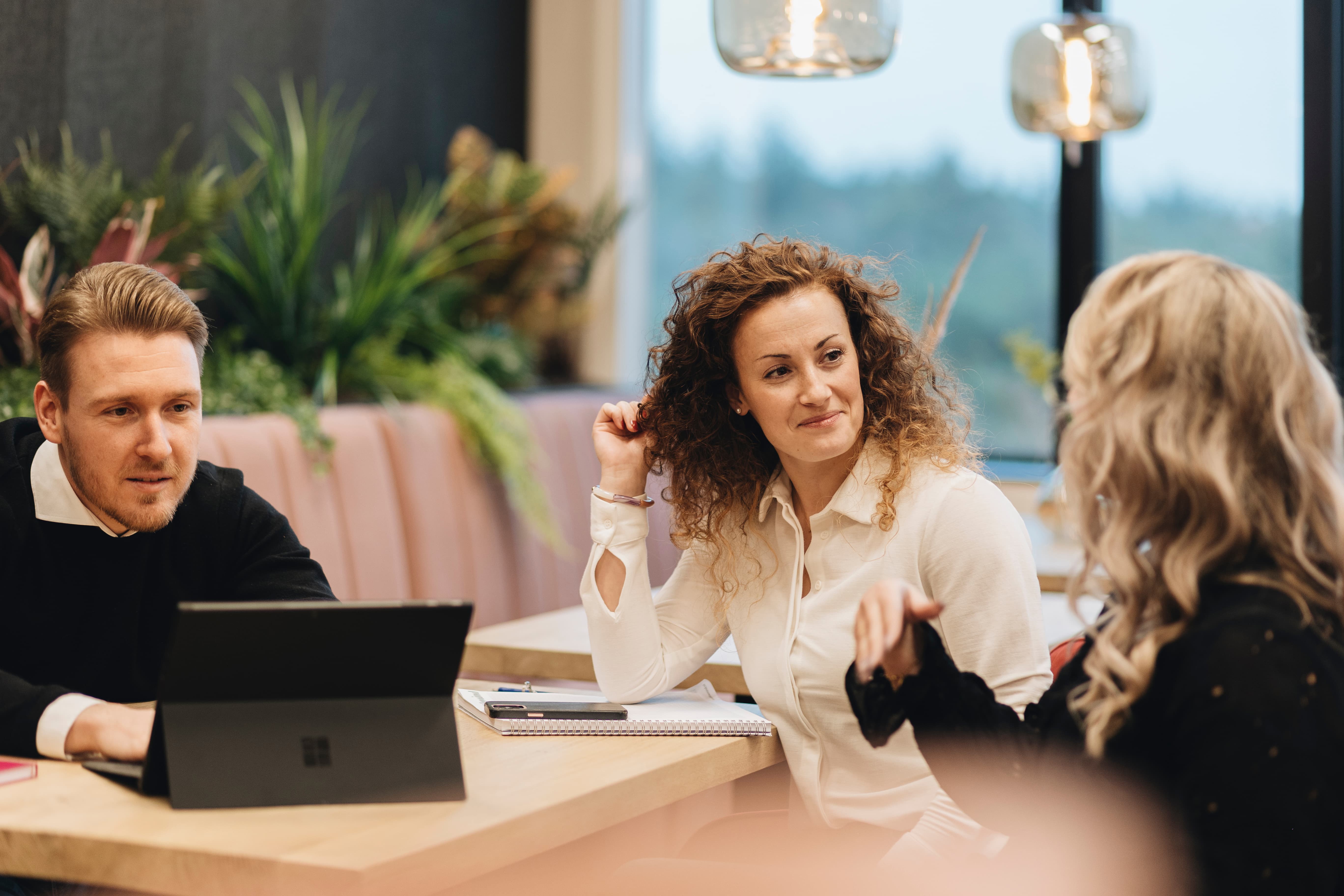 One man in front of a computer while two women discuss something at the same table.