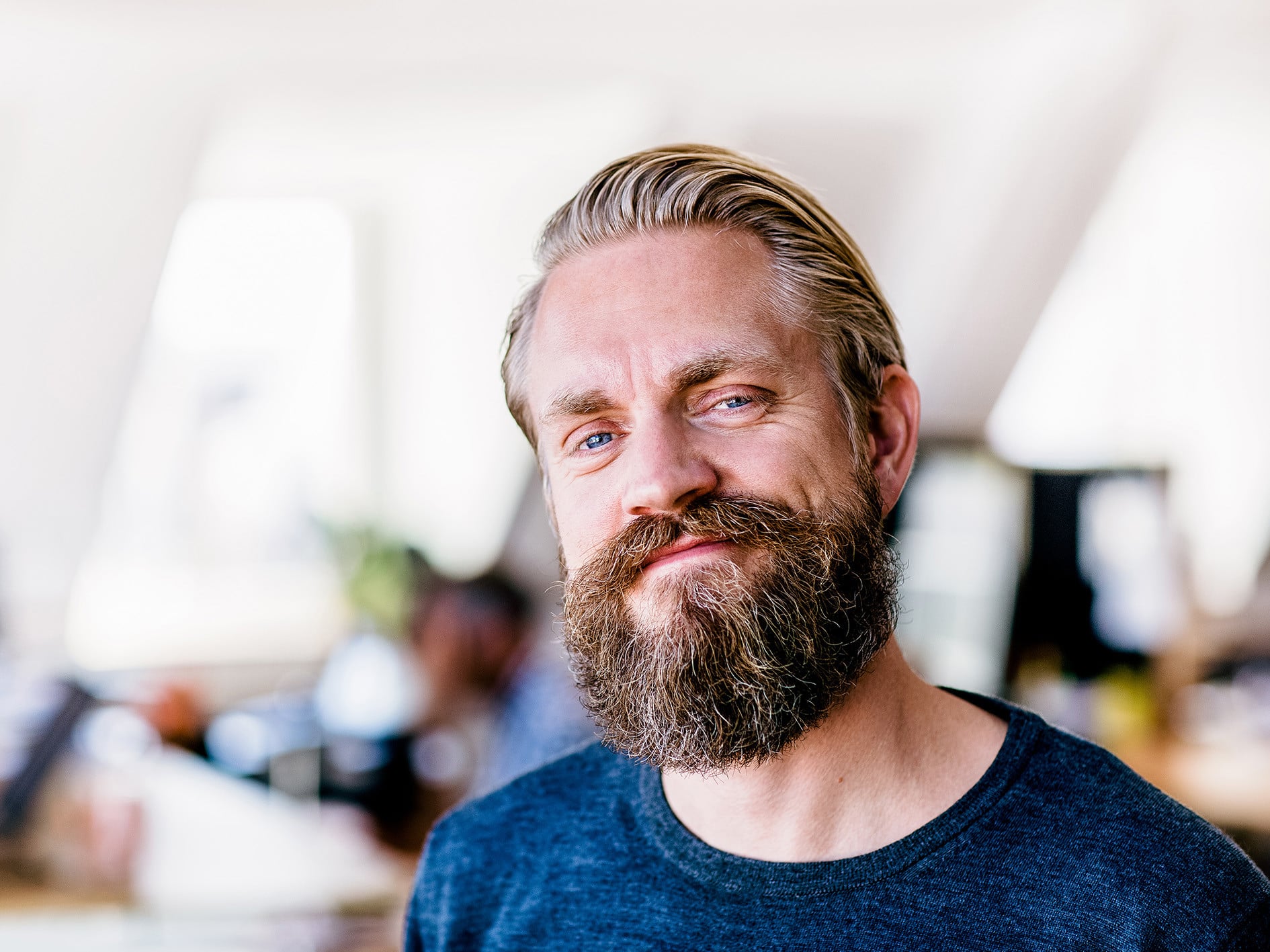 Portret van een man met baard in een kantooromgeving, met collega’s op de achtergrond