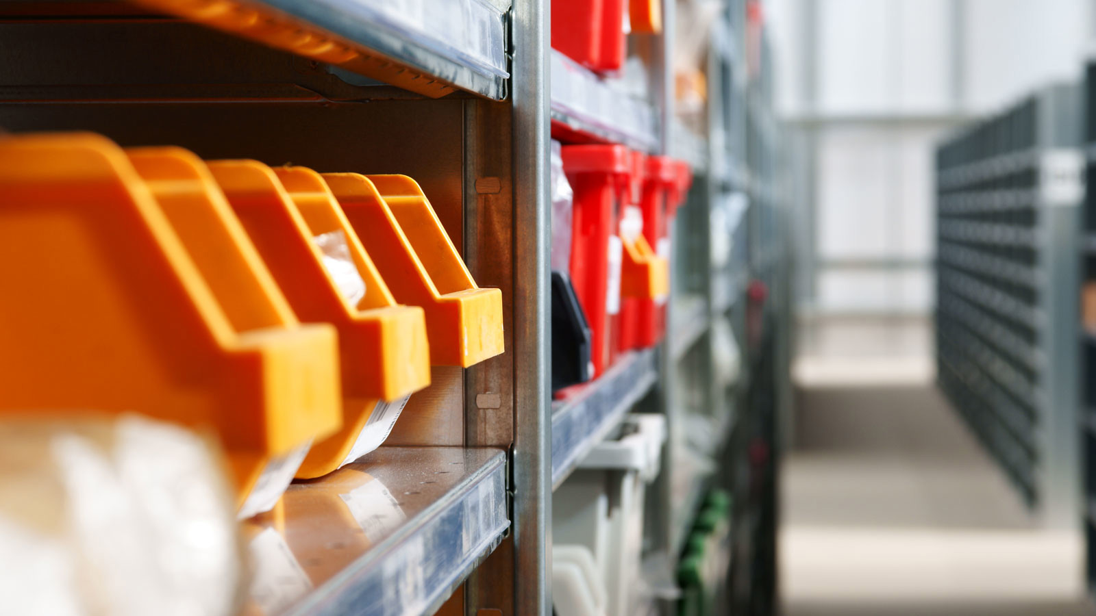 Orange och röda plastlådor i lagerhyllor i ett förråd eller lager. Fokus på organiserad förvaring och logistik